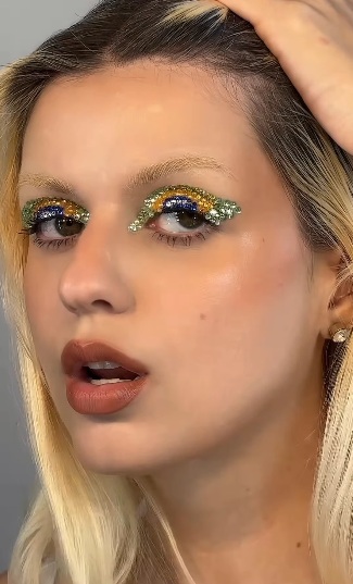 Mulher branca e loira com maquiagem para a copa e strass coloridos nos olhos, que reproduzem a bandeira do Brasil