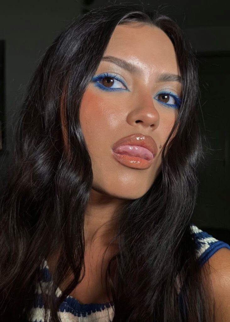 Mulher branca com cabelo preto com maquiagem para a copa e delineado azul.