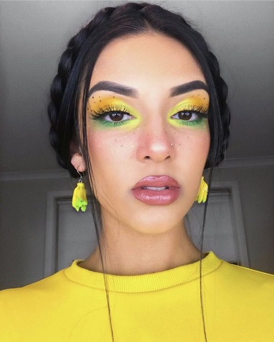 Mulher branca com cabelo castanho preso com maquiagem para a copa nas cores amarelo e verde.