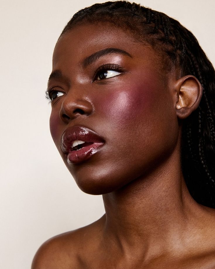 Mulher negra séria, com rosto na lateral, lábios levemente abertos, com maquiagem para pele negra.
